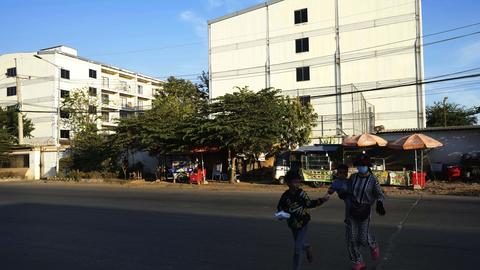 A family runs across the street near a building, where some people trafficked under false pretenses are forced to work in online scams targeting people all over the world, in Phnom Penh, Cambodia, Sunday, Feb. 9, 2025. (AP Photo/Heng Sinith)