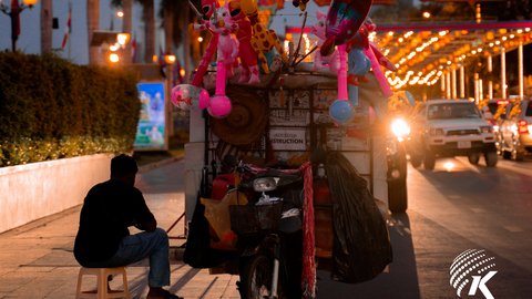 A lone balloon vendor sits by the riverside, bathed in the night's glow. Kiripost/Van Chan Thada